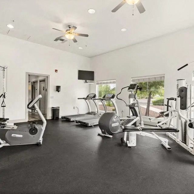 A spacious gym with treadmills, elliptical machines, and a fan.