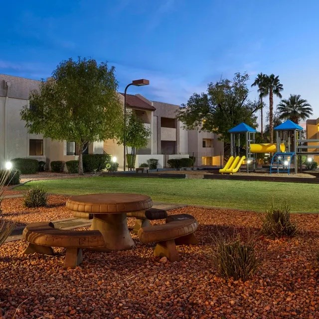 A playground with a slide and a picnic table is lit up at dusk.