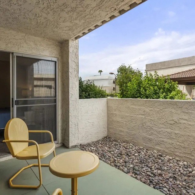 A yellow chair and table are on a patio with a view of a building and trees.
