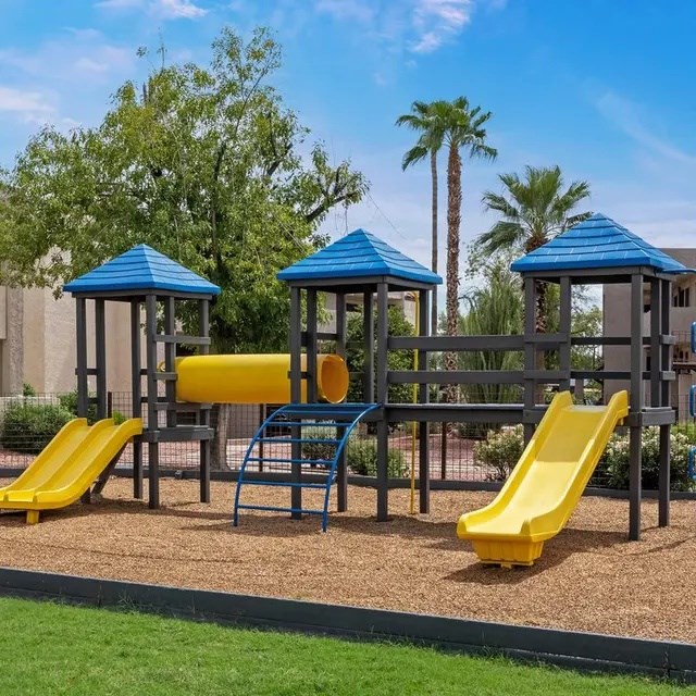 A playground with a yellow slide and blue roofed structures.