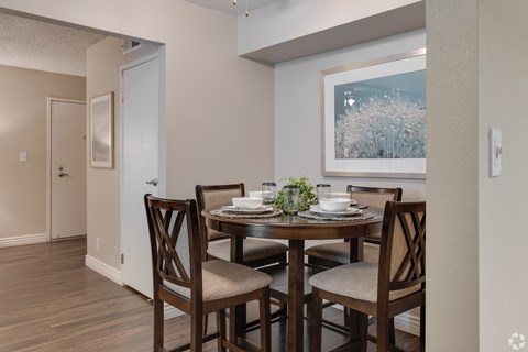 A dining room with a table set for two and a painting on the wall.