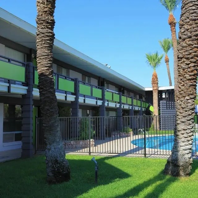 A building with a pool and palm trees in front.
