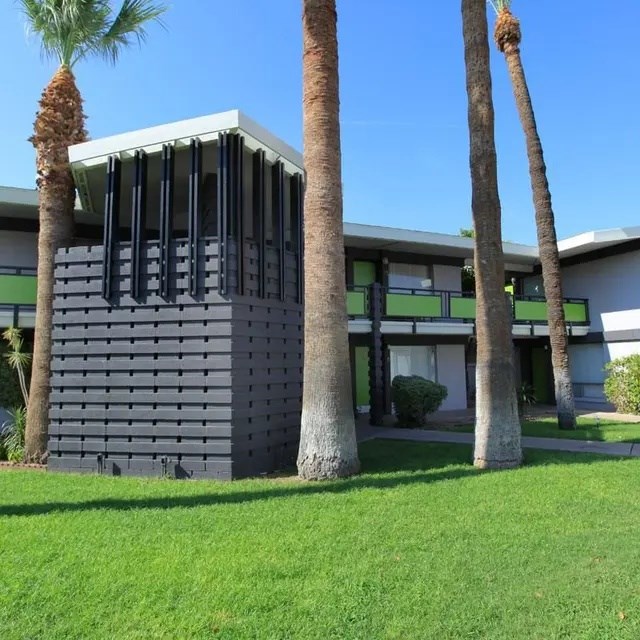A modern building with a flat roof and a grey facade is surrounded by palm trees.