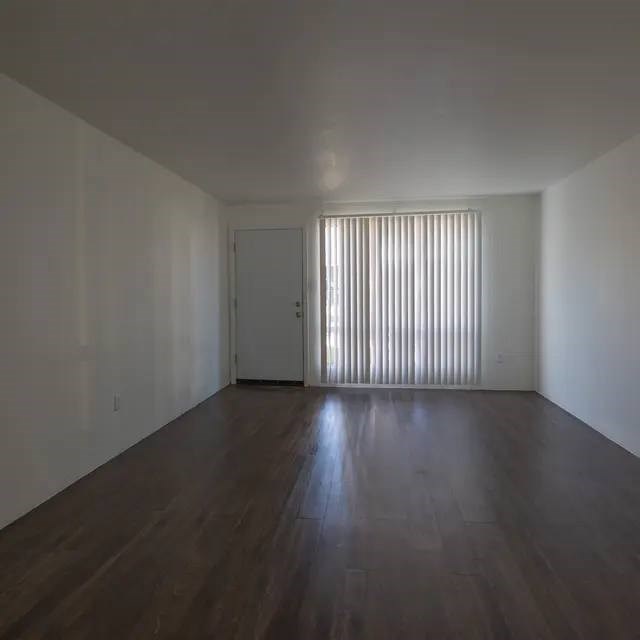 A room with wooden floors and a door with blinds on the window.