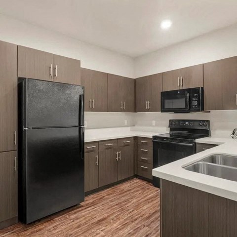 A black refrigerator stands in a kitchen with wooden cabinets and a black oven.