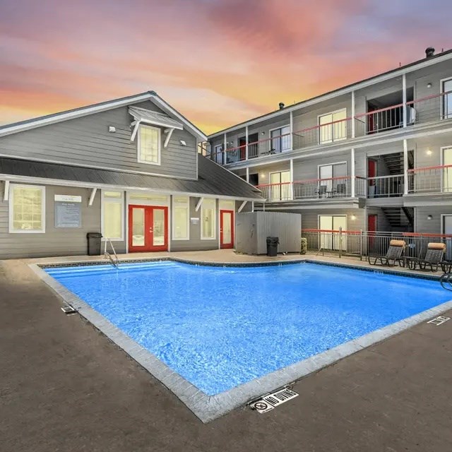 A swimming pool in front of a building with a sunset in the background.