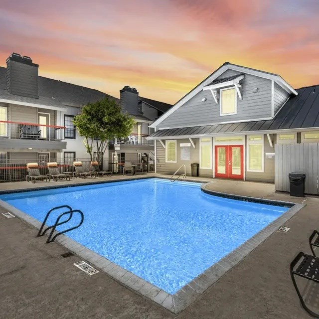 A swimming pool in front of a house with a sunset in the background.