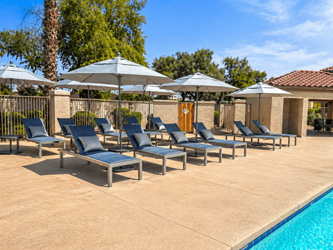 A row of lounge chairs are arranged in a row by a pool.