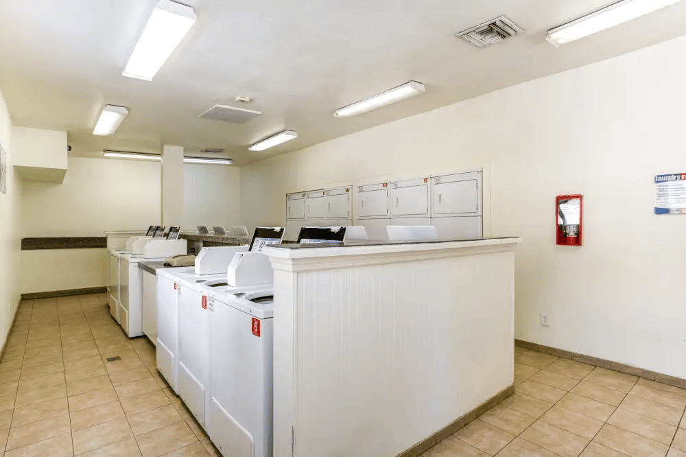 A clean, white-walled laundry room with a row of washers and dryers.