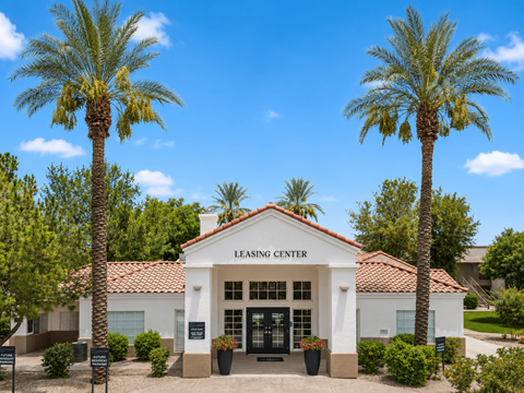 A white building with a red tile roof and a sign that says "Leasing Center" is surrounded by palm trees.