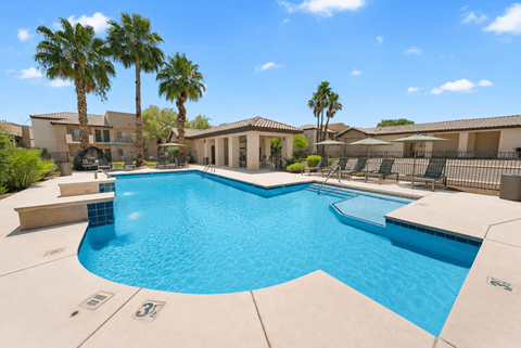 A large swimming pool surrounded by palm trees and a building.