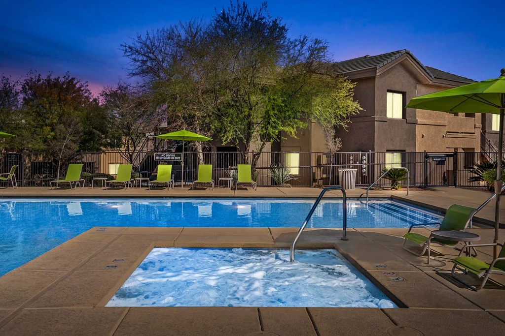 A swimming pool surrounded by chairs and umbrellas at dusk.