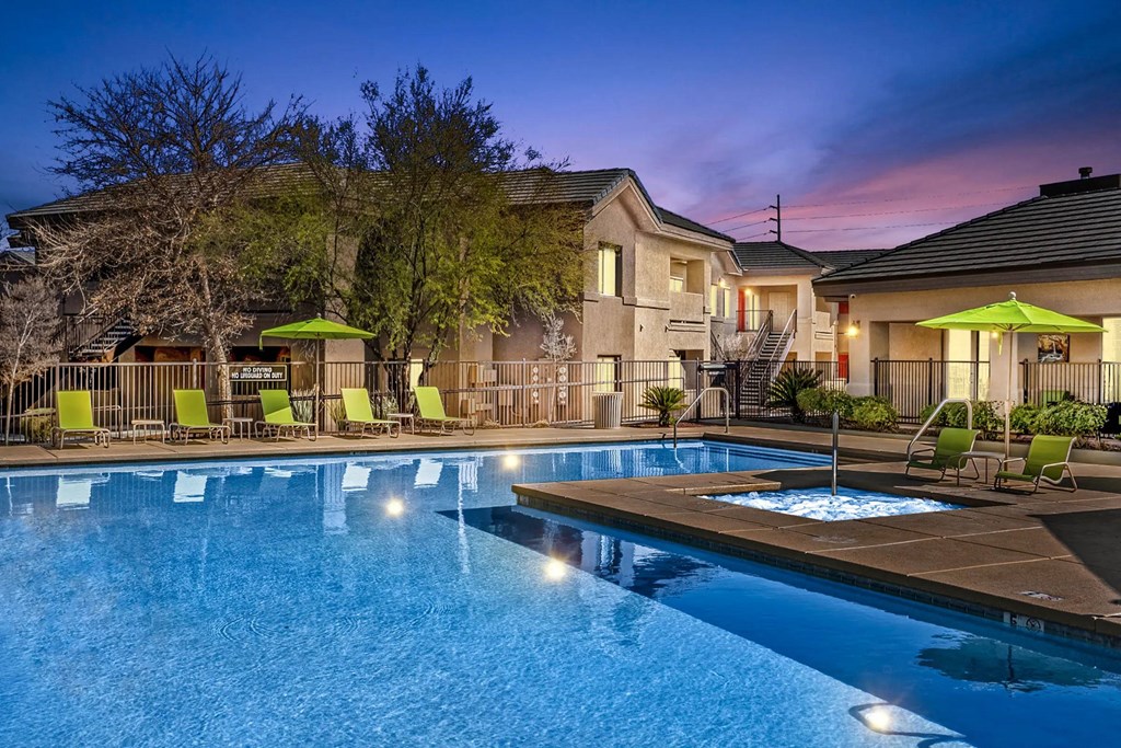 A swimming pool surrounded by lounge chairs and umbrellas at dusk.