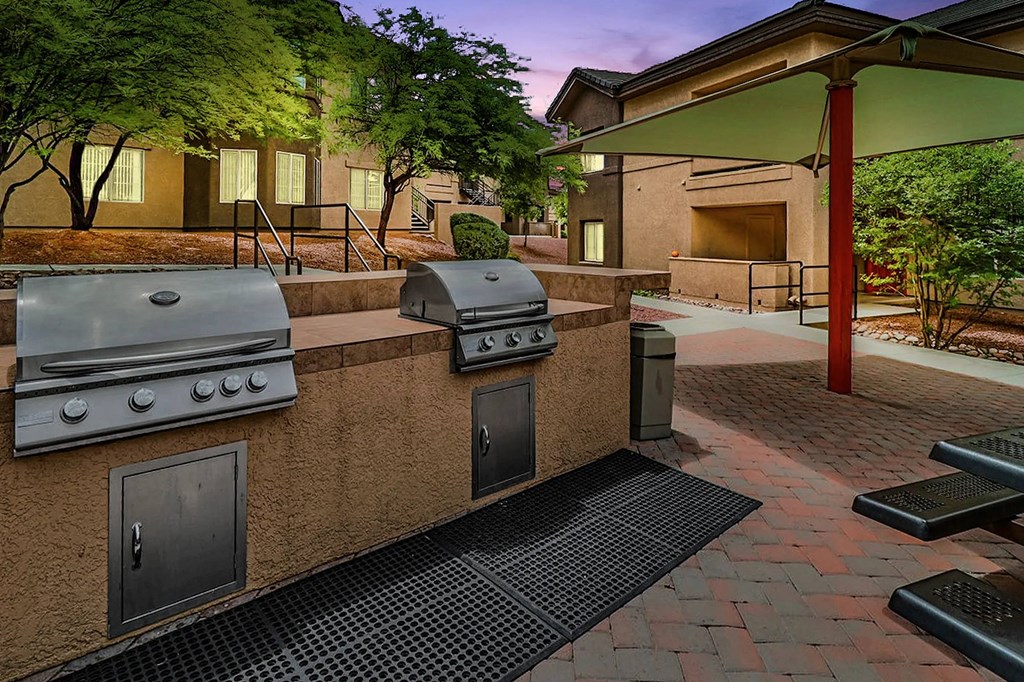 A patio with a grill and picnic tables.