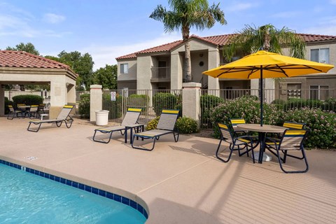 A pool area with a table and chairs and a yellow umbrella.