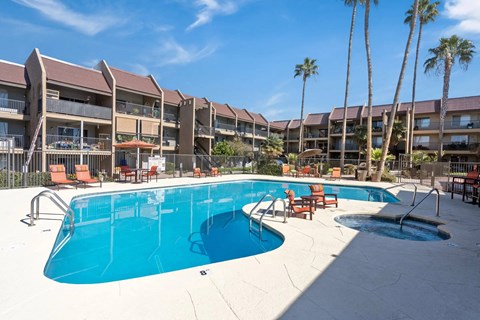A large swimming pool in front of apartment buildings with palm trees.