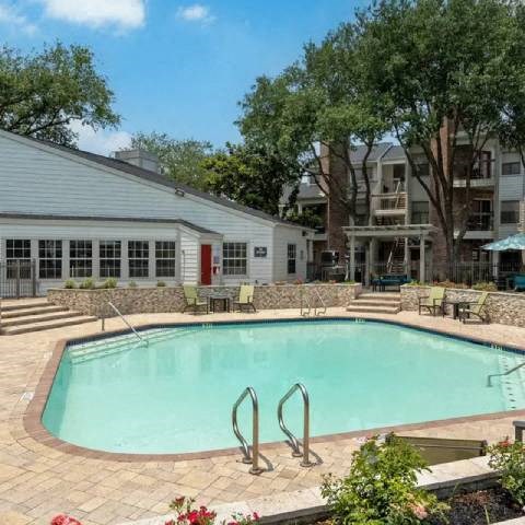 A swimming pool surrounded by a stone wall and a patio area with chairs and a table.