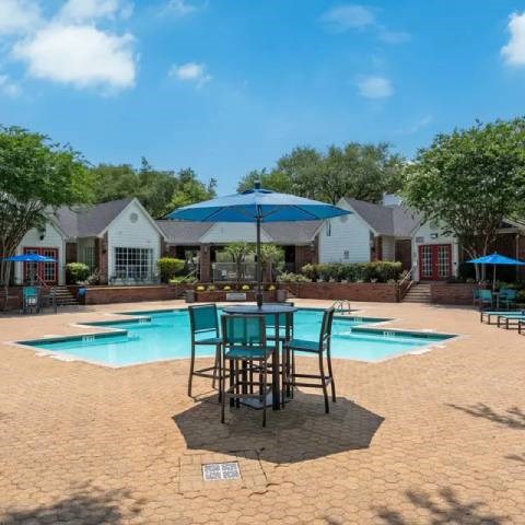 A pool area with a table and chairs and umbrellas.
