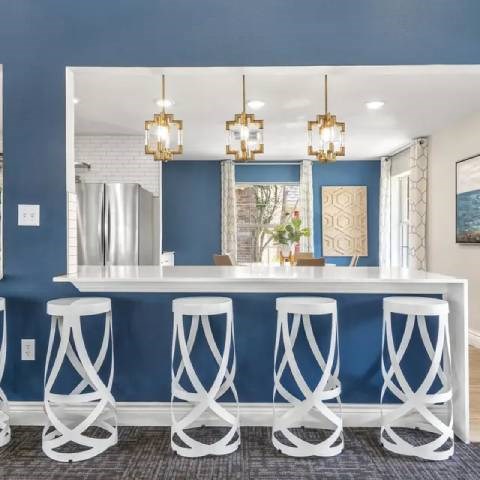 A bar with white stools and a mirror above it.