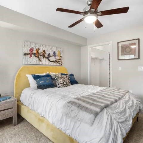 A bedroom with a bed, a ceiling fan, and a painting on the wall.
