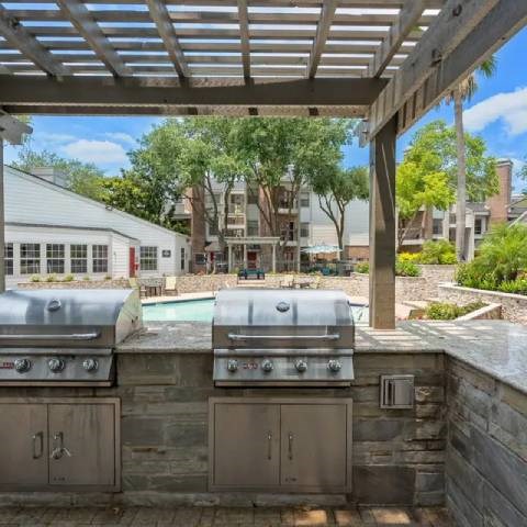Two grills are on a patio with a pool in the background.