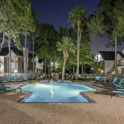 A swimming pool surrounded by palm trees and lounge chairs at night.