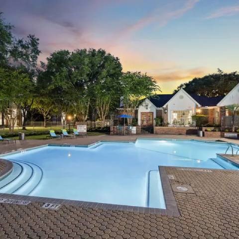A large outdoor swimming pool surrounded by trees and a building in the background.