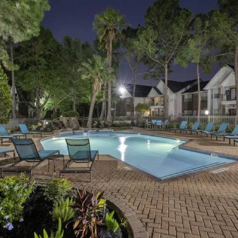 A pool surrounded by trees and chairs at night.