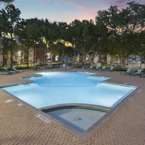 A large outdoor swimming pool surrounded by trees and lounge chairs.