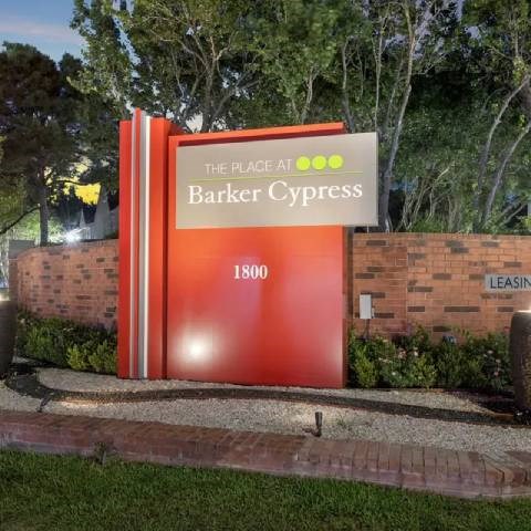 A sign for Barker Cypress is displayed in front of a brick wall.