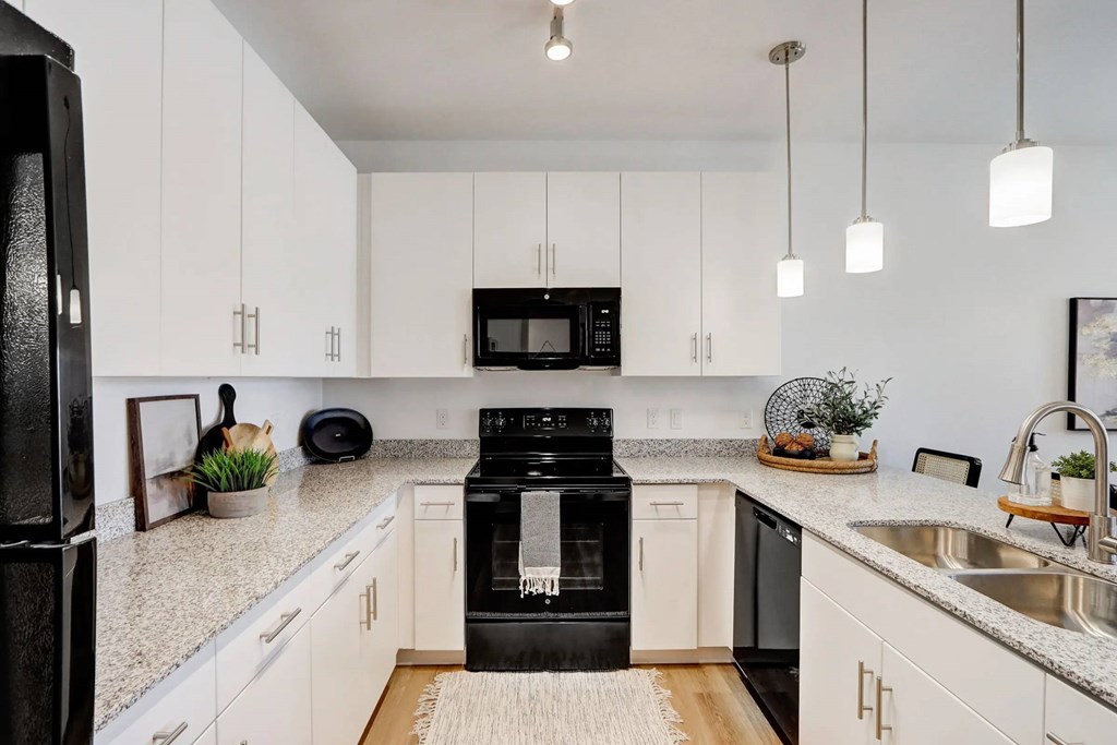 A black refrigerator is in a kitchen with white cabinets.