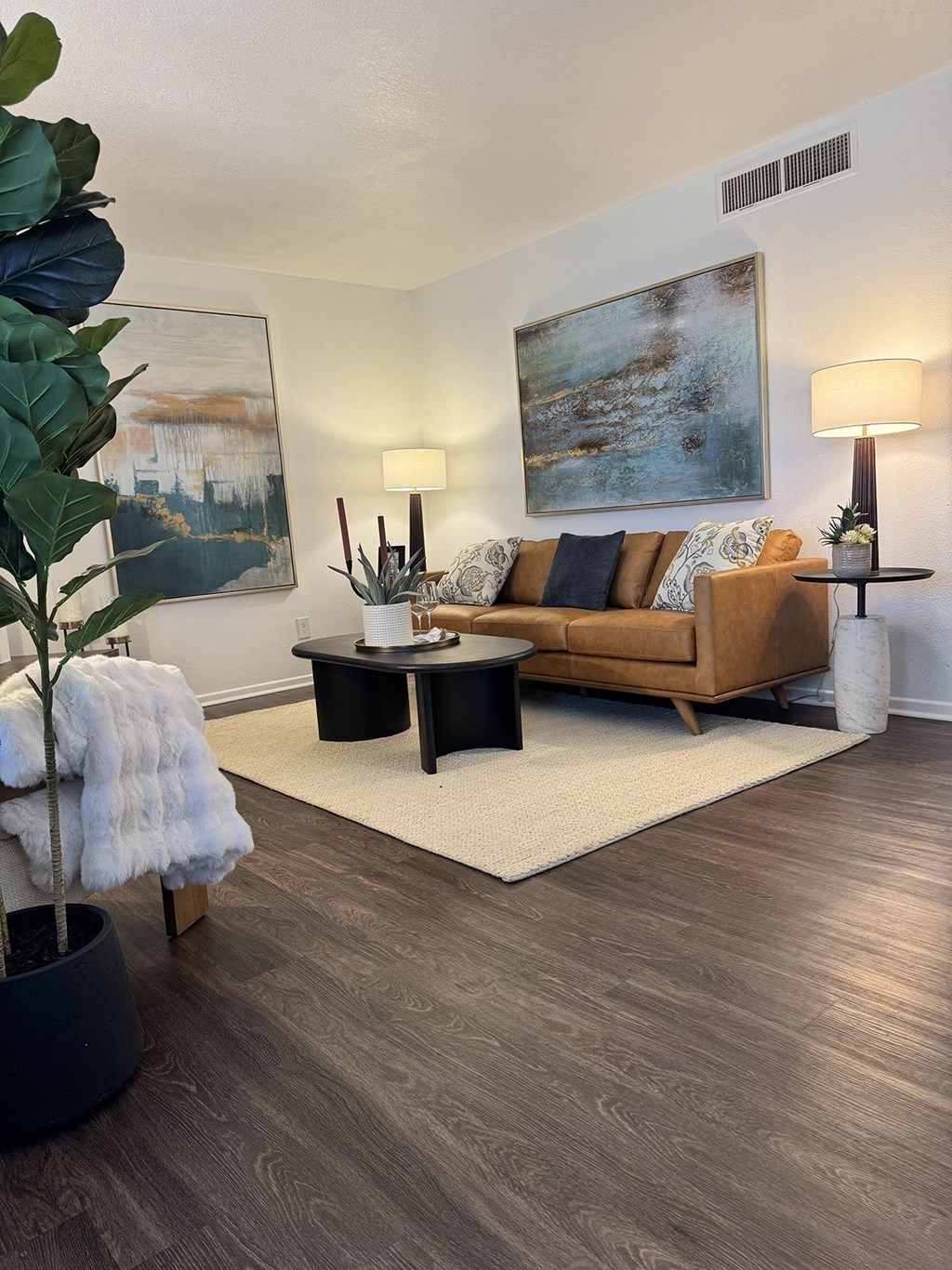 A living room with a brown couch, a white rug, and a painting on the wall.