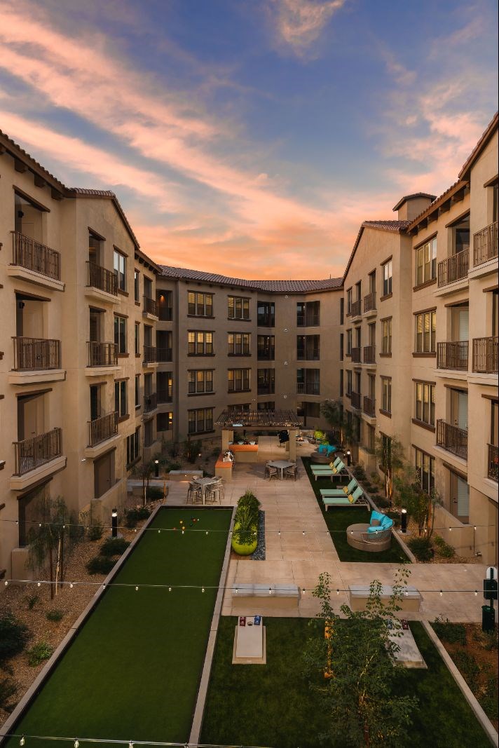 A sunset view of a courtyard with a green lawn and apartment buildings.