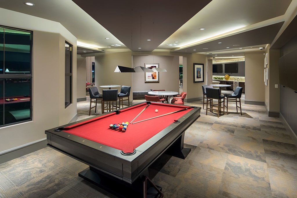 A pool table is in the middle of a room with a bar and a dining table.
