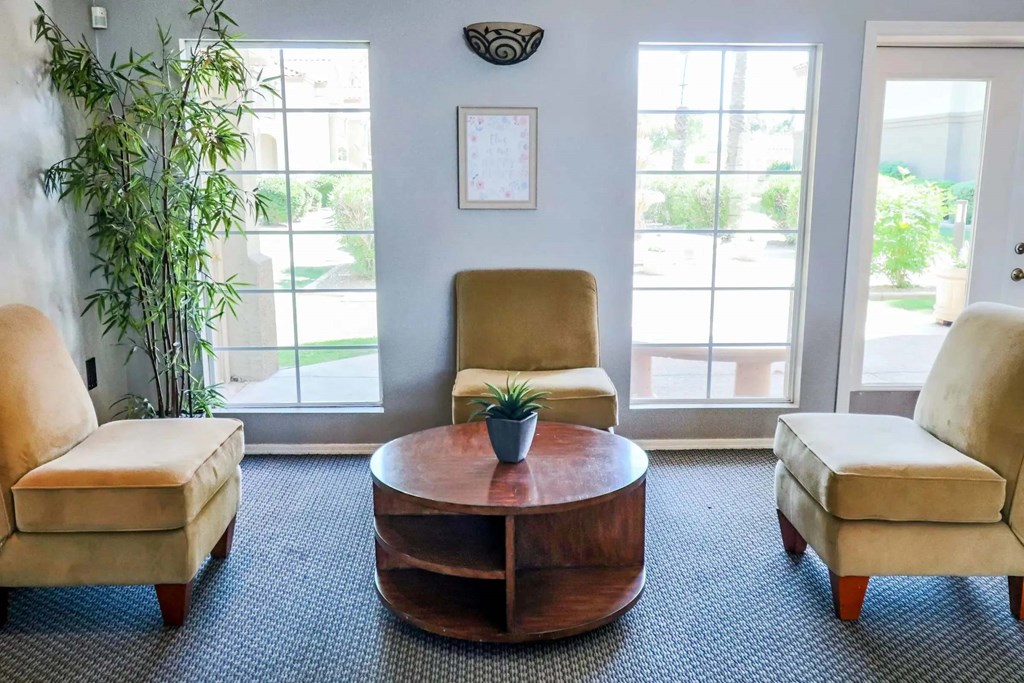 A living room with a brown coffee table, two tan chairs, and a potted plant.