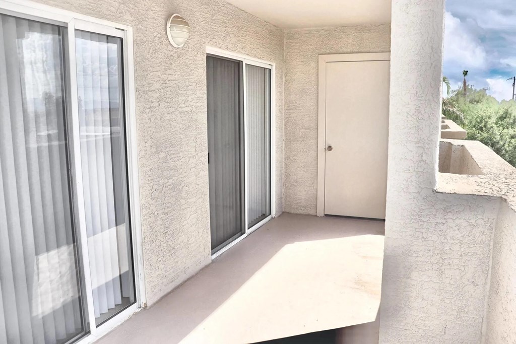 A balcony with a white door and grey window blinds.