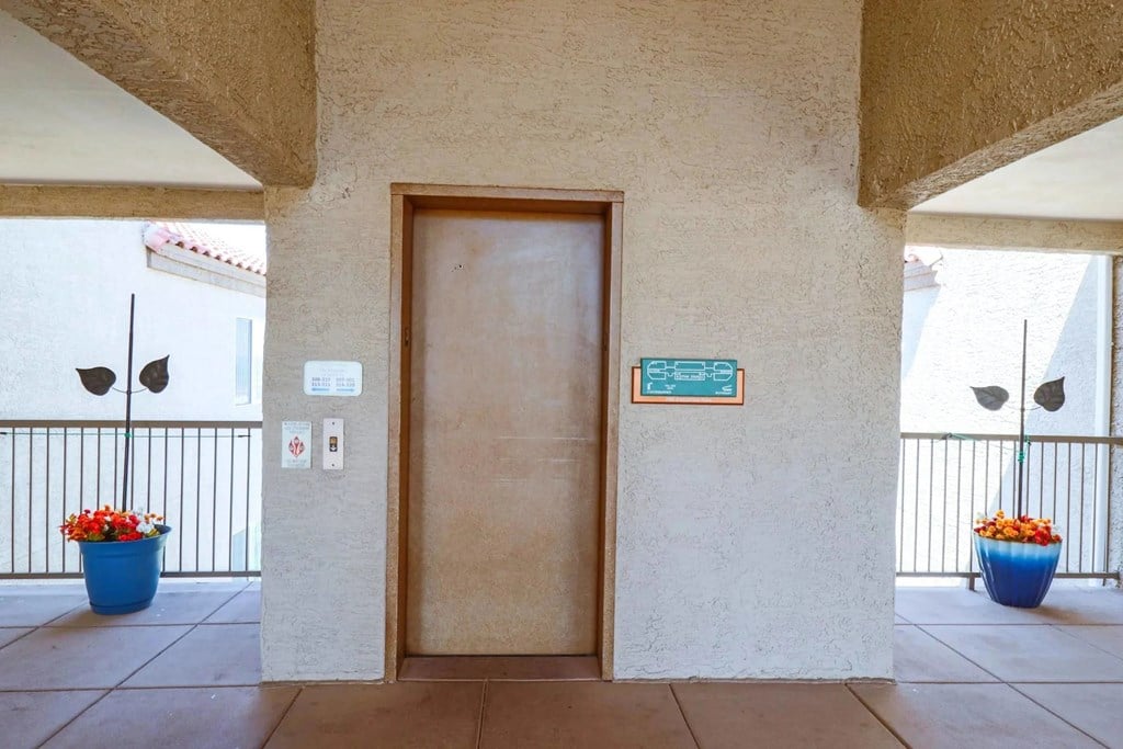 A brown door with a plaque above it and two blue pots with flowers on either side.