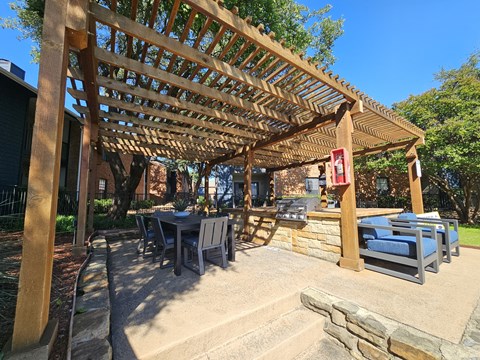 A wooden pergola with a table and chairs underneath it.