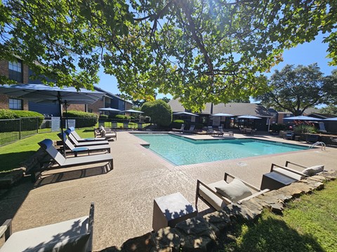 A pool surrounded by lounge chairs and trees.