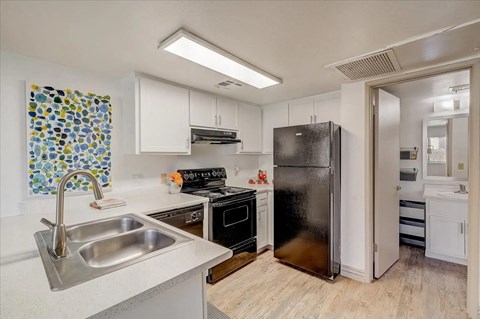 A kitchen with a black refrigerator and a sink with a silver faucet.
