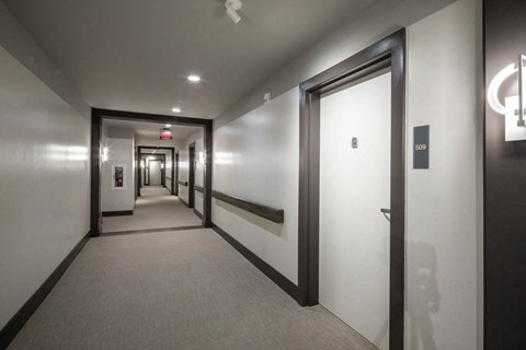 A hallway with a carpeted floor, white walls, and a series of doors on the right side.