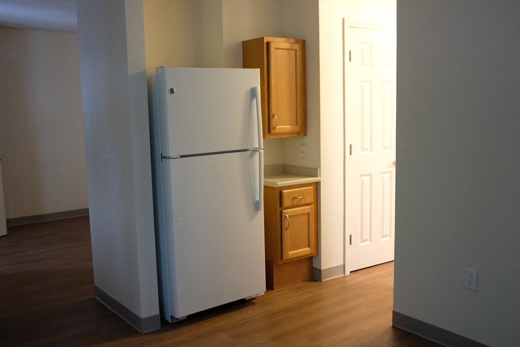 an empty kitchen with a white refrigerator and wooden floors