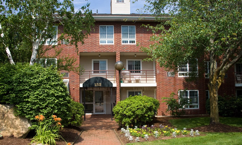 the front of a red brick apartment building with a sidewalk and trees