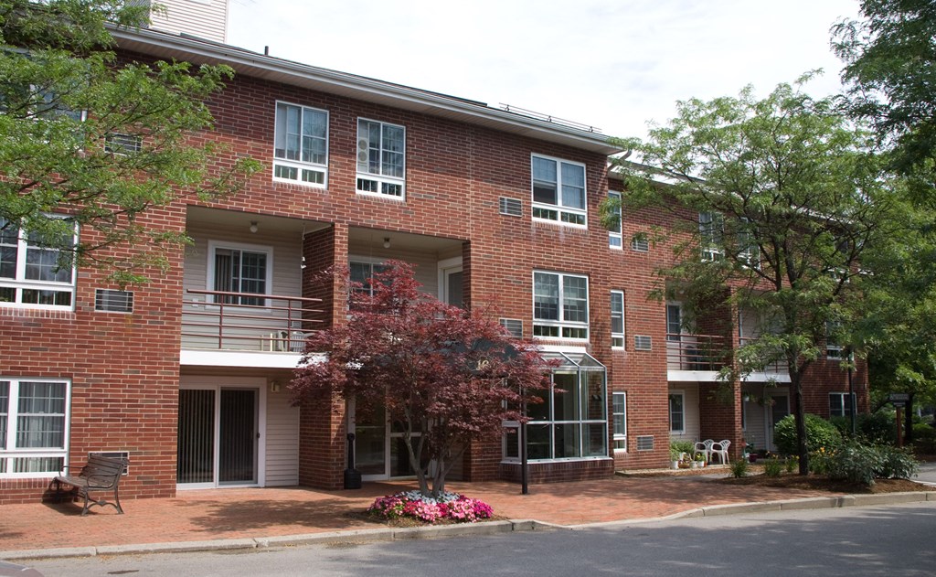 a red brick apartment building with a porch and a tree