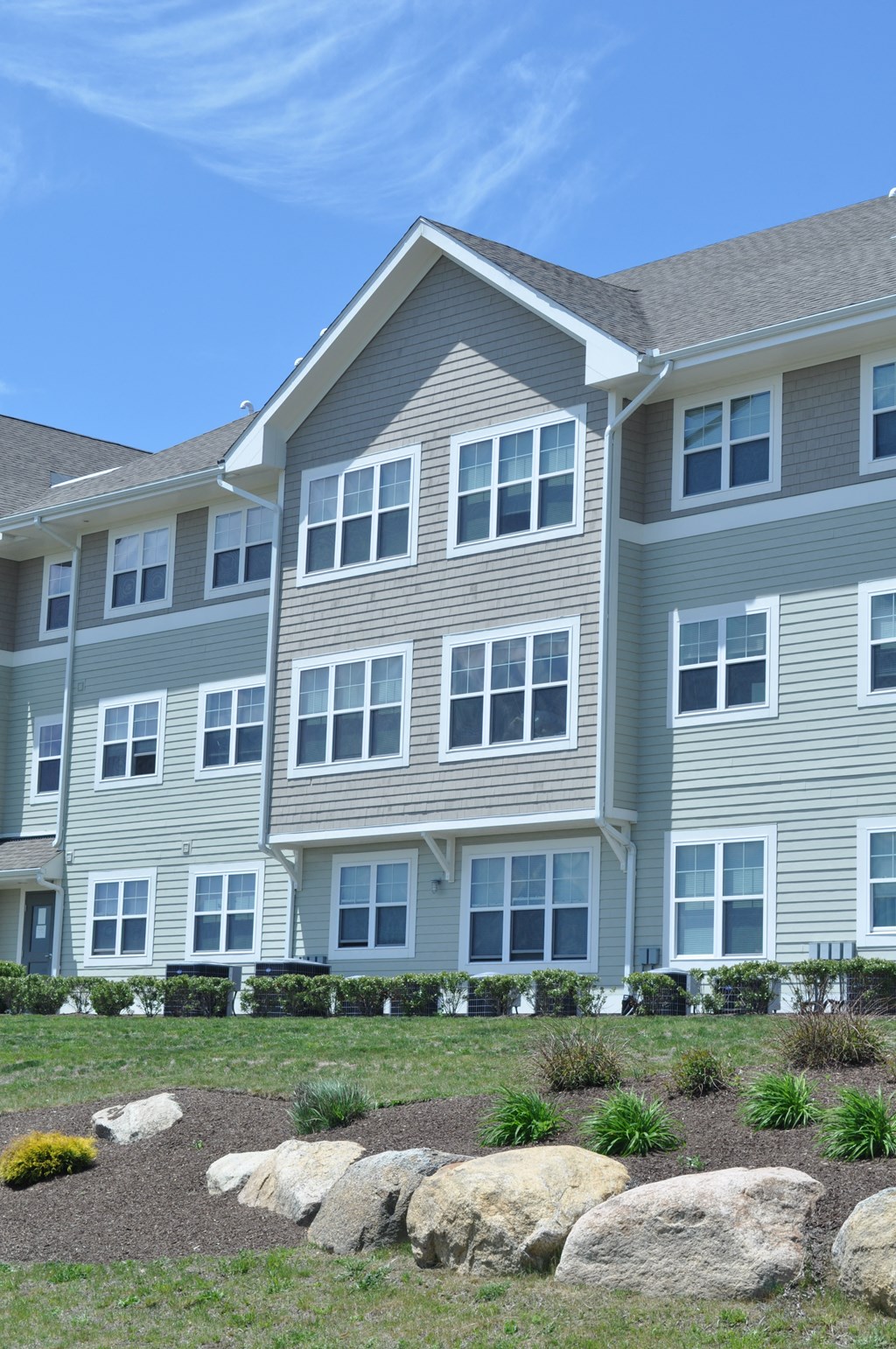 a large apartment building with a lawn and rocks in front of it