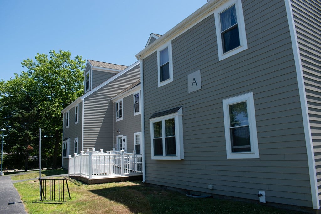 a gray house with a white porch and a white fence