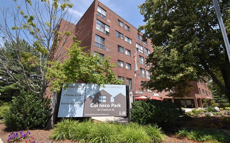 A sign for Cocheco Park in front of a brick building.
