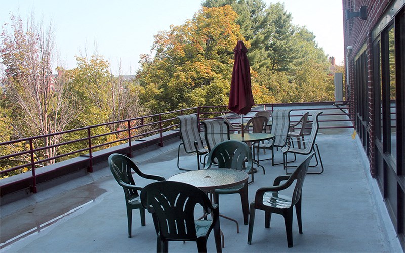 A patio with chairs and tables is surrounded by trees.