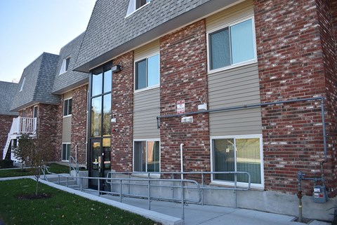 A red brick building with a grey roof and a metal railing in front.