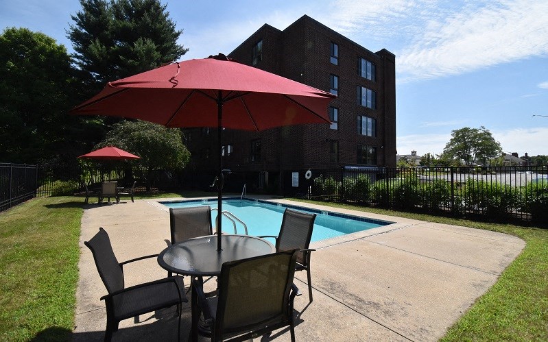 A red umbrella is on a table next to a pool.